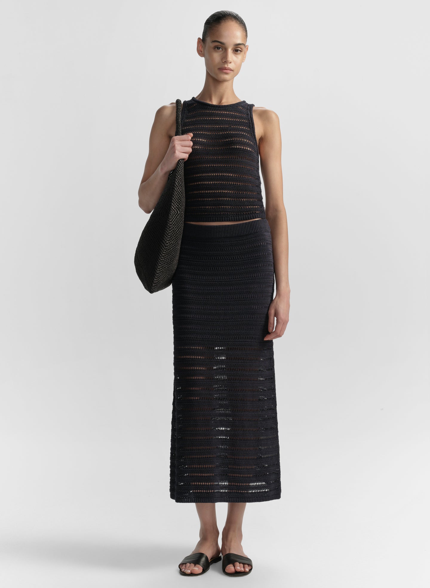 Woman wearing a blue sleeveless top and long skirt holding a matching bag on a white background