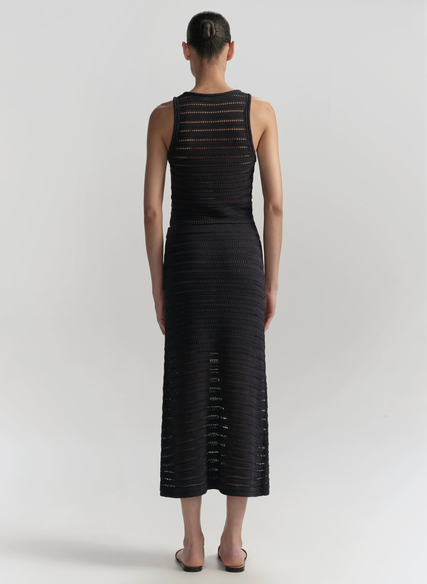 Woman wearing a bllue sleeveless top with skirt with textured pattern on a white background