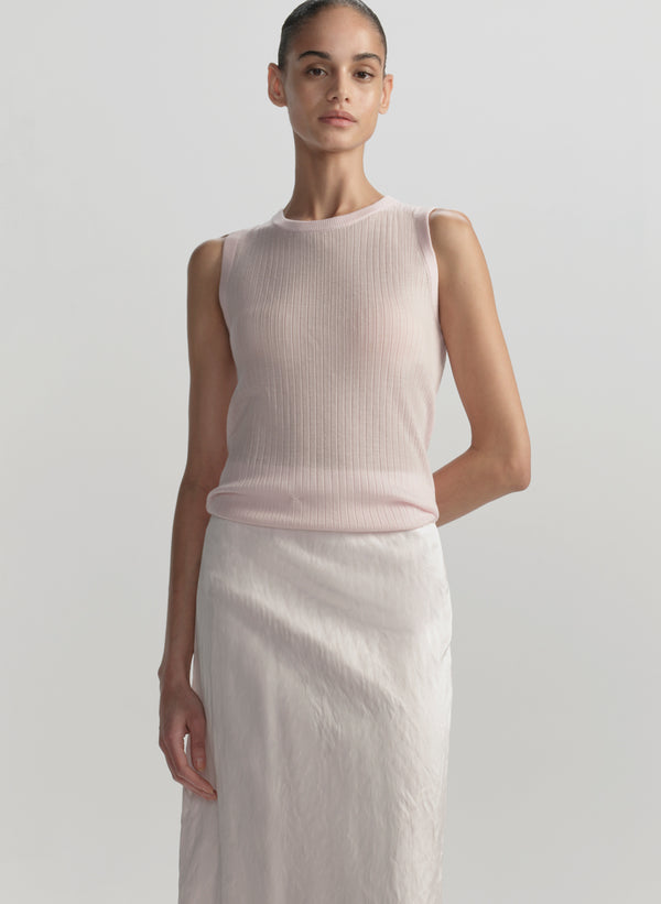 Woman wearing a light pink sleeveless top and white pants against a plain background