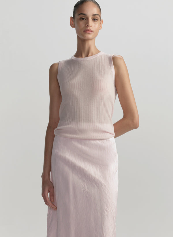 Woman wearing a light pink sleeveless top and skirt on a plain background