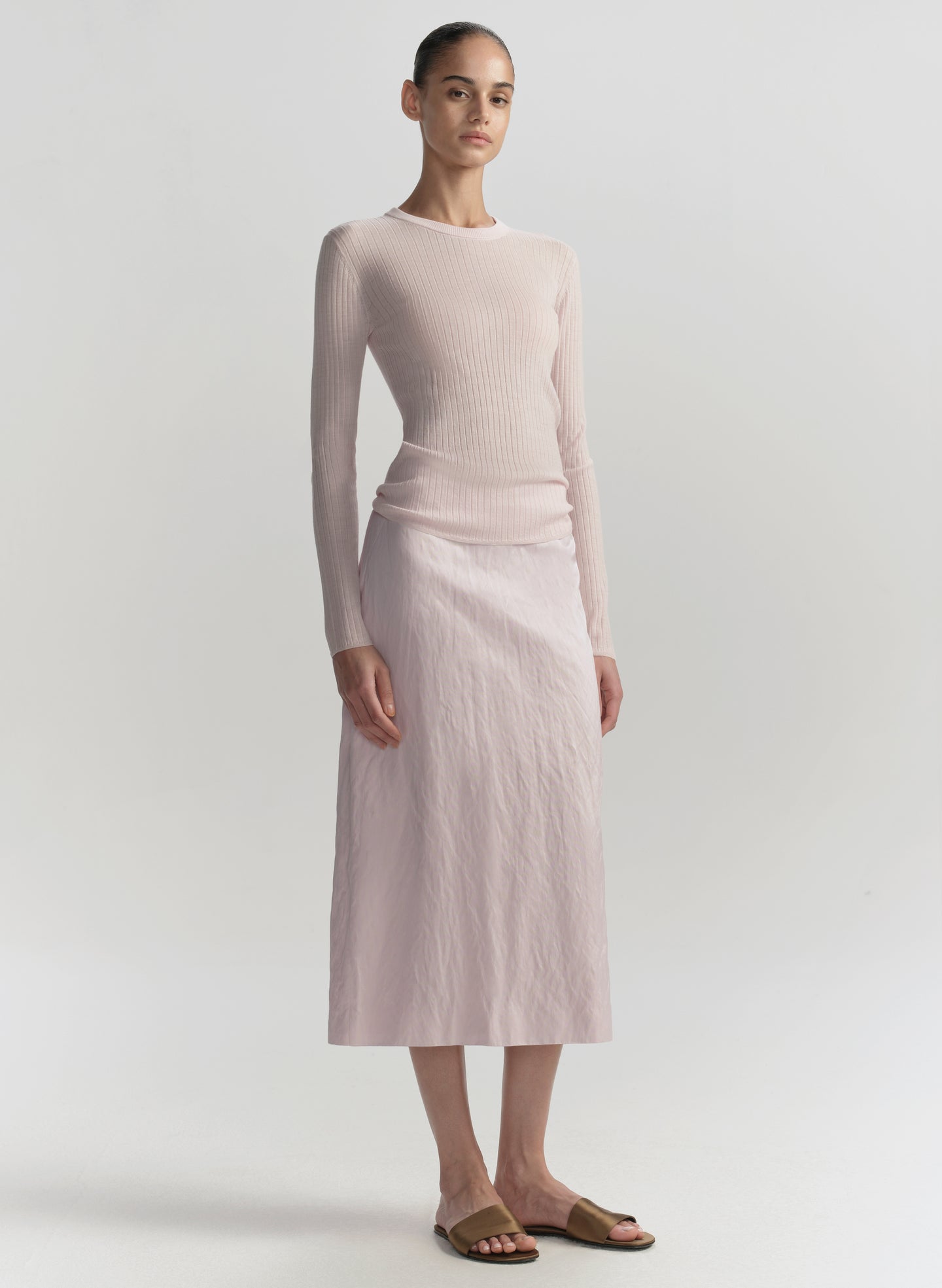 Woman wearing a light pink ribbed sweater and matching skirt on a white background