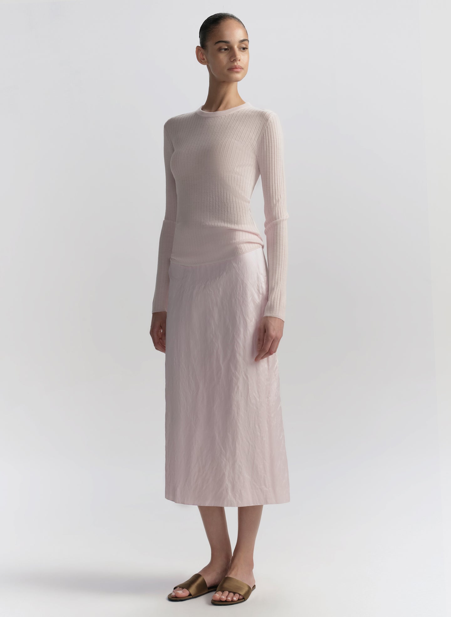 Woman wearing a light pink ribbed sweater and skirt set on a white background