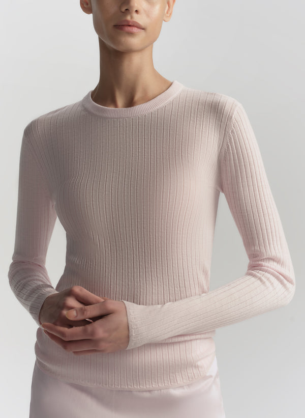 Person wearing a light pink ribbed sweater against a plain background