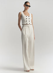 Woman wearing a white sleeveless top with buttons and wide-leg pants on a light gray background
