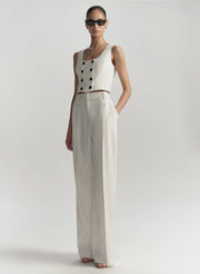 Woman wearing a white sleeveless top with buttons and wide-leg pants on a plain background