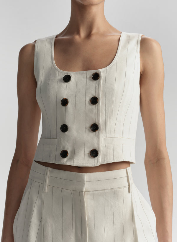 White sleeveless top with black buttons on a plain background