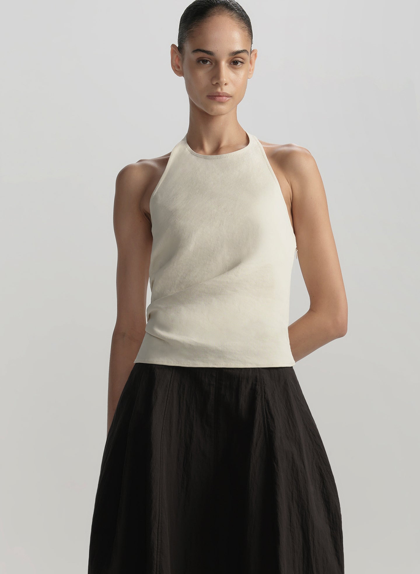 Woman wearing a beige sleeveless top and black skirt on a light gray background
