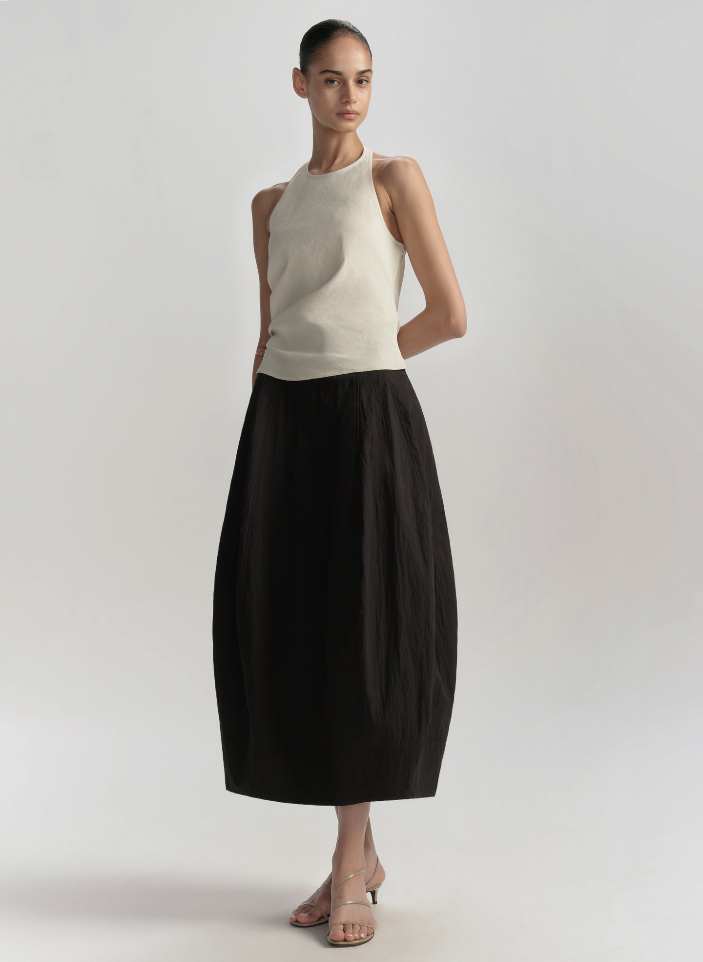 Woman wearing a beige sleeveless top and black skirt on a plain background