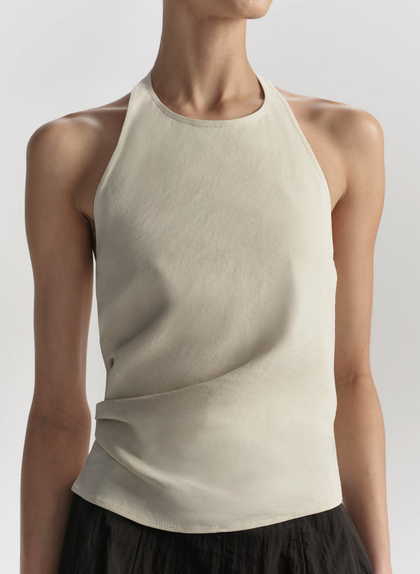 Woman wearing a beige sleeveless top with a plain background