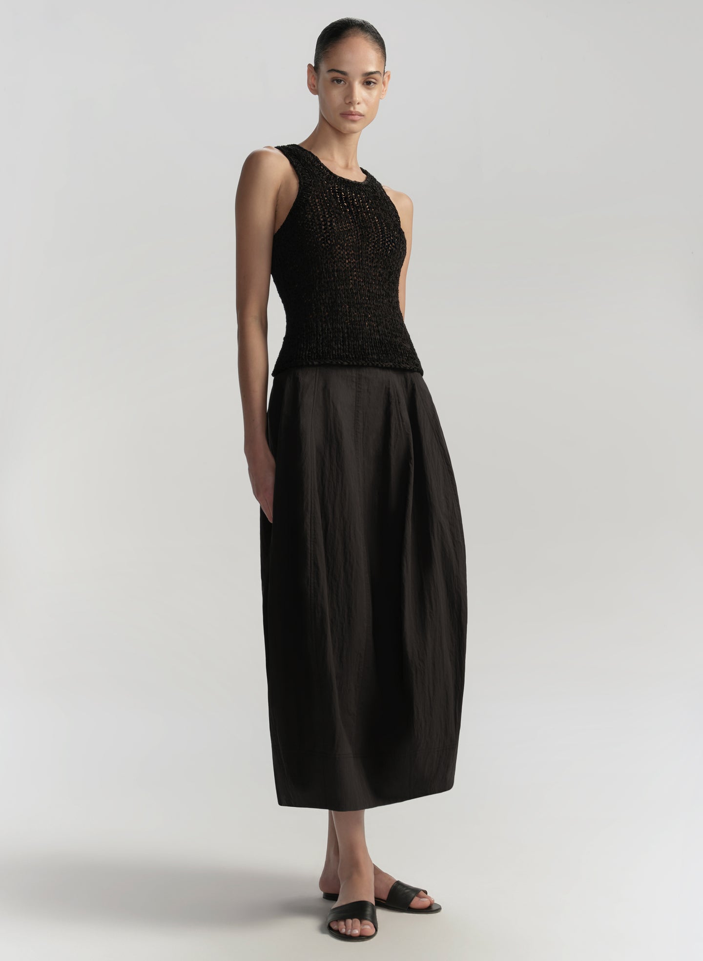 Woman wearing a black sleeveless top and long black skirt on a light gray background