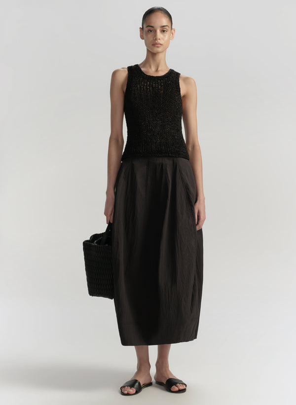 Woman wearing a black sleeveless top and black skirt on a white background