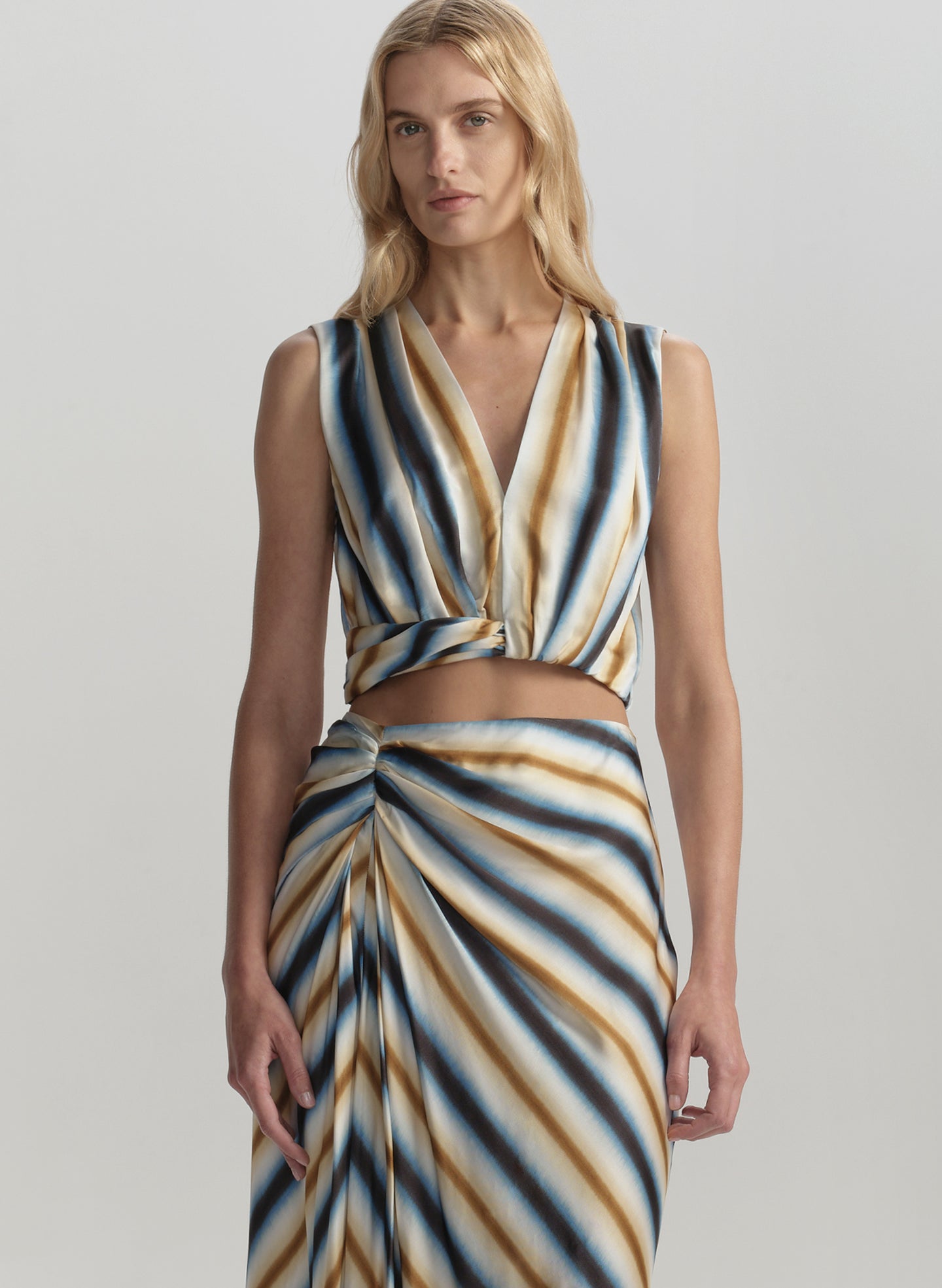 Woman wearing a sleeveless, striped dress with a V-neckline on a plain background