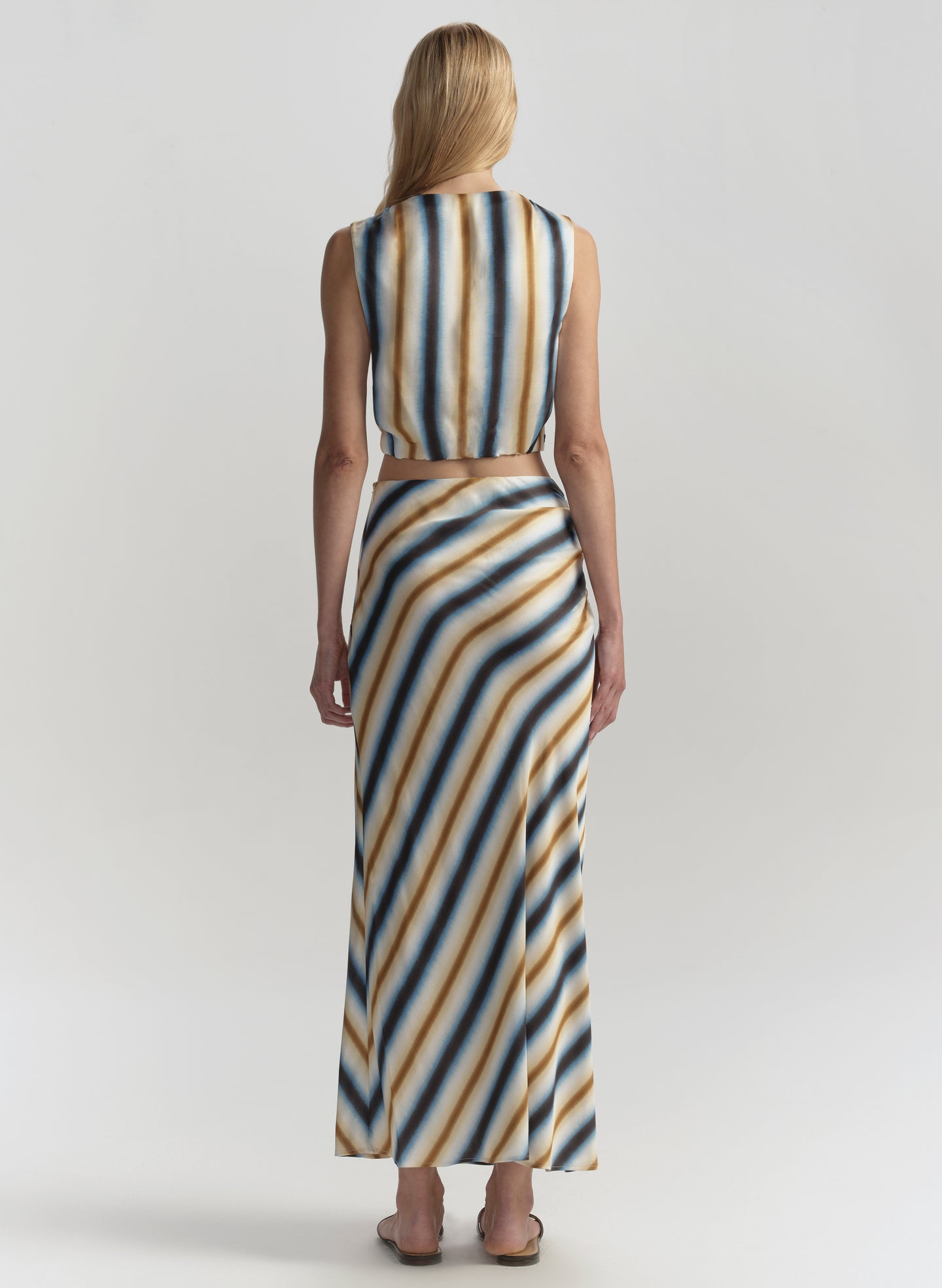 Woman wearing a sleeveless striped top and long skirt on a plain background