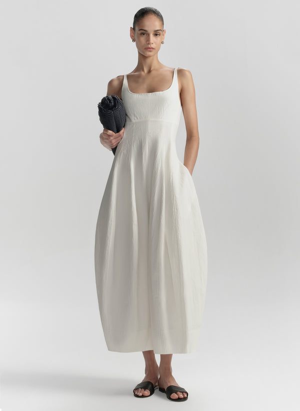 Woman wearing a white dress holding a blue clutch against a plain background