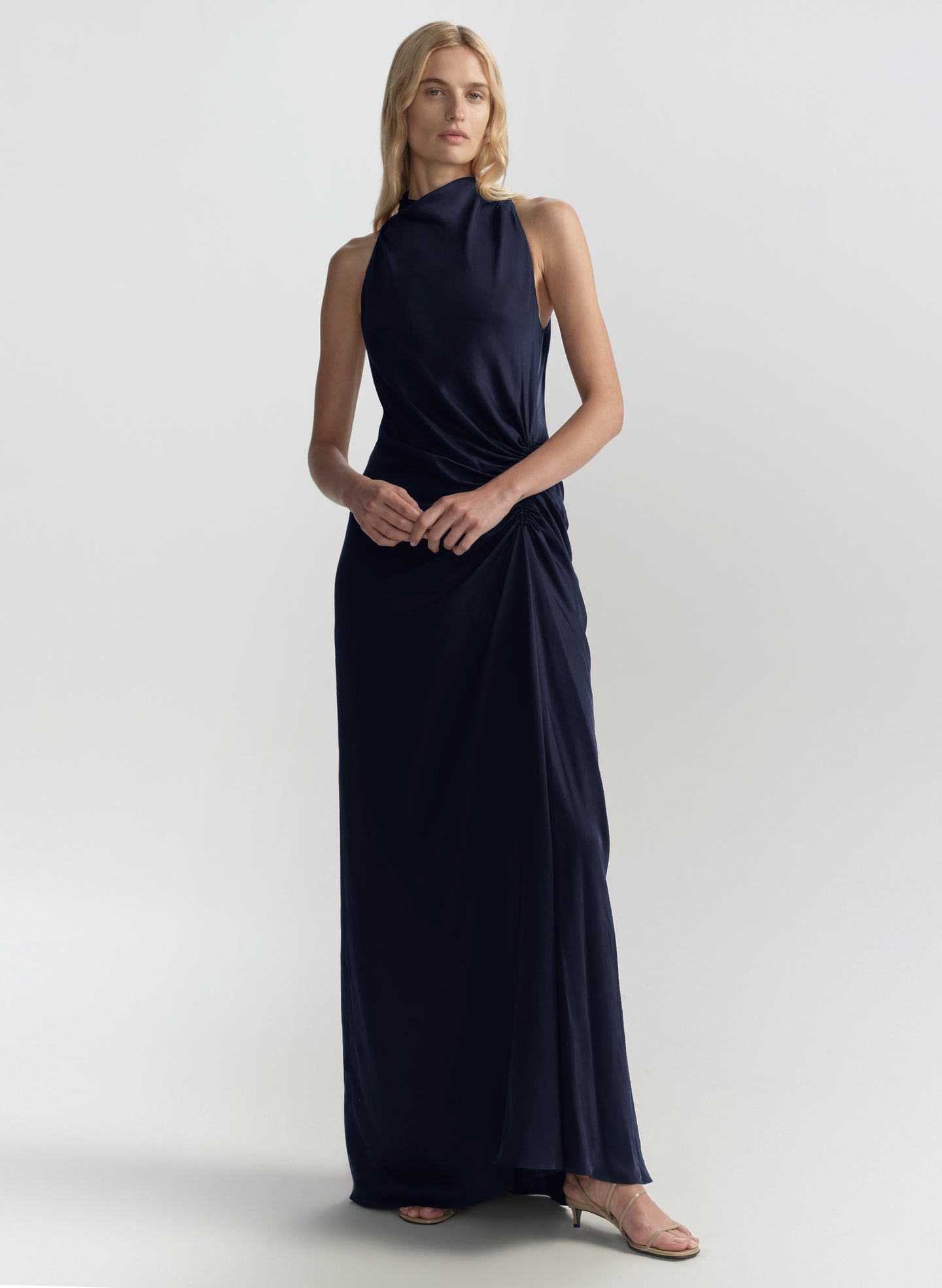 Woman wearing a navy blue halter neck gown on a light gray background