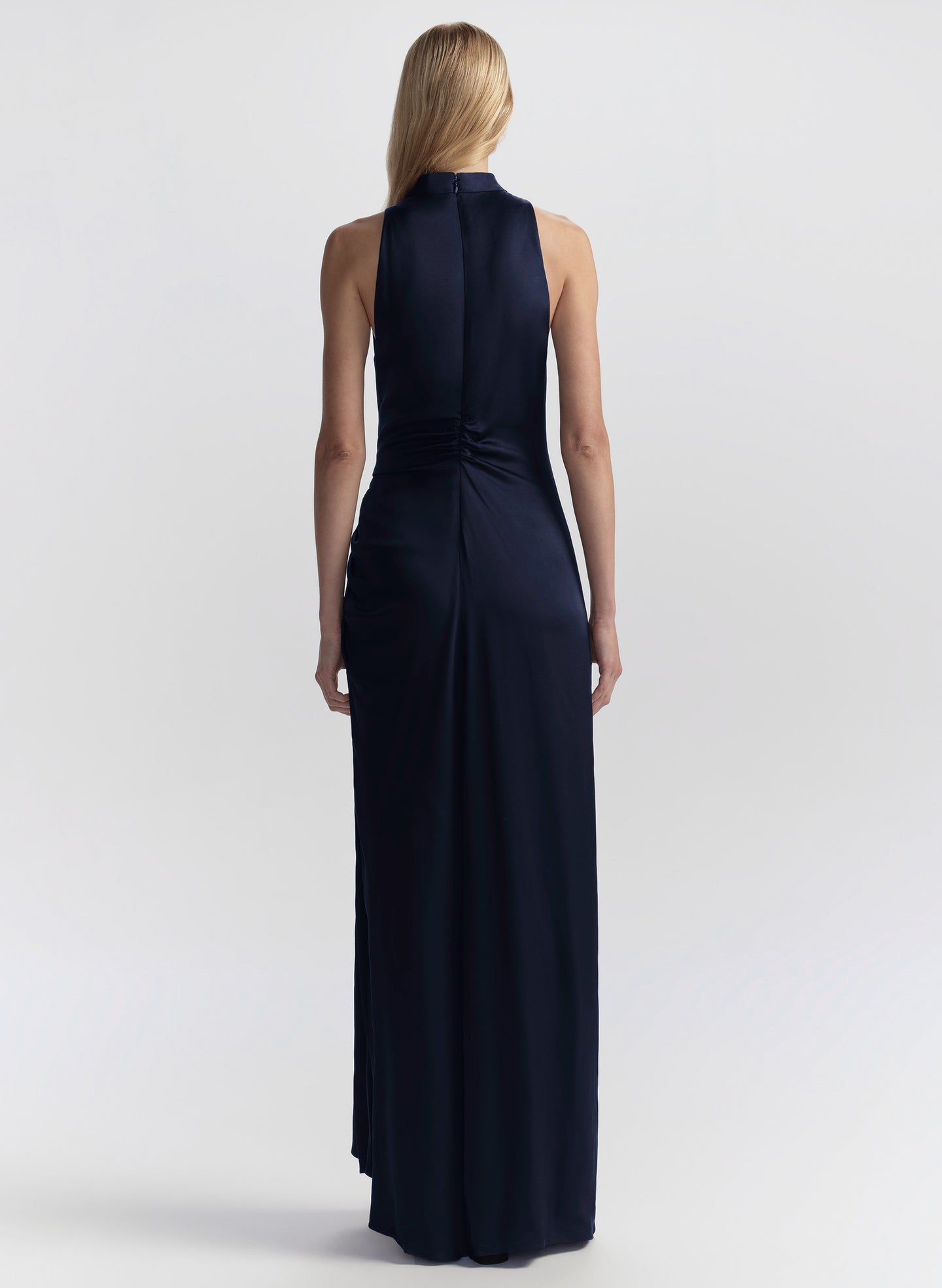 Woman wearing a navy blue halter neck gown on a light gray background