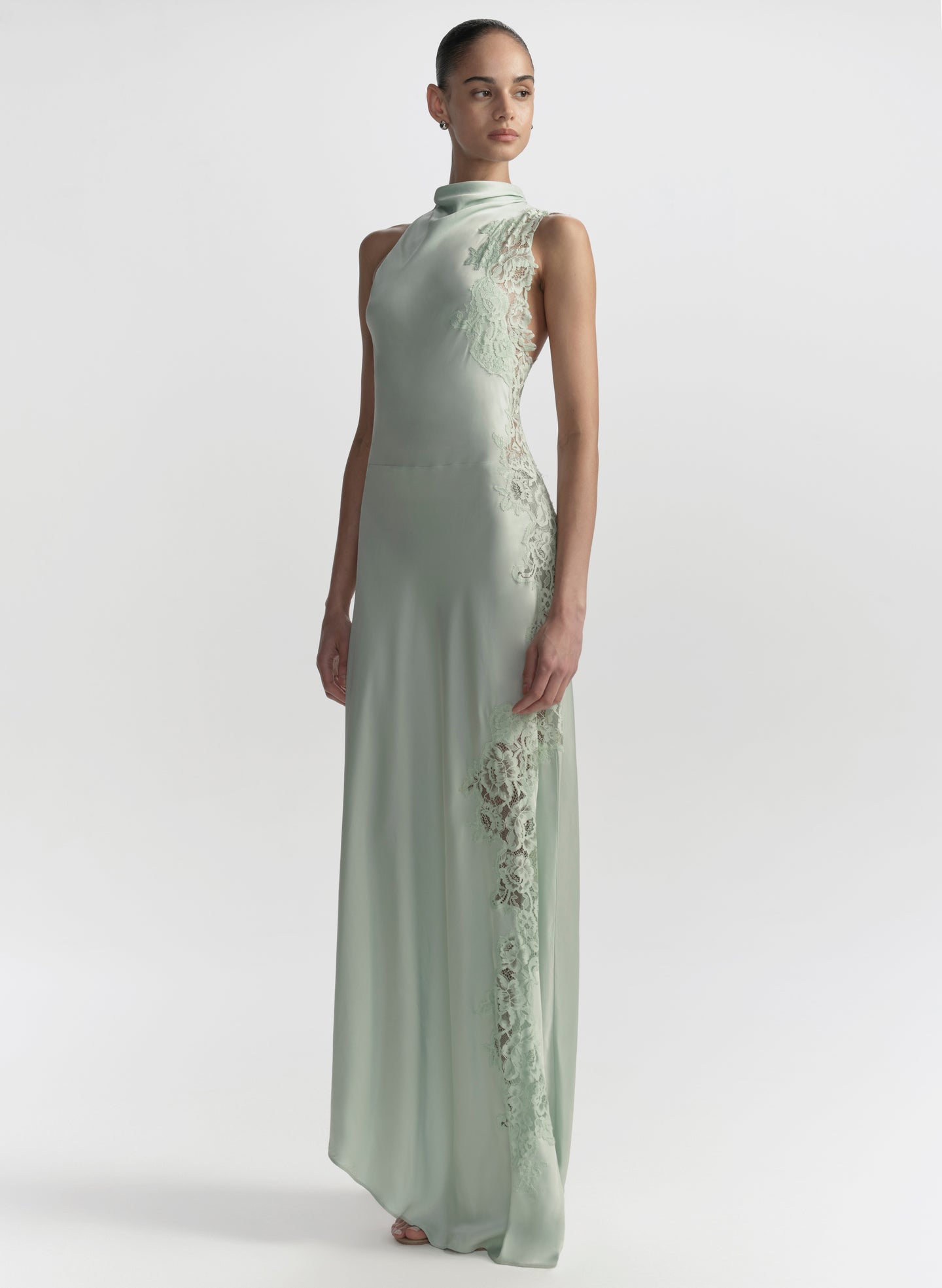 Woman wearing a light green evening gown with floral embroidery on a white background