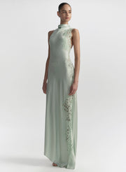 Woman wearing a light green evening gown with floral embroidery on a white background