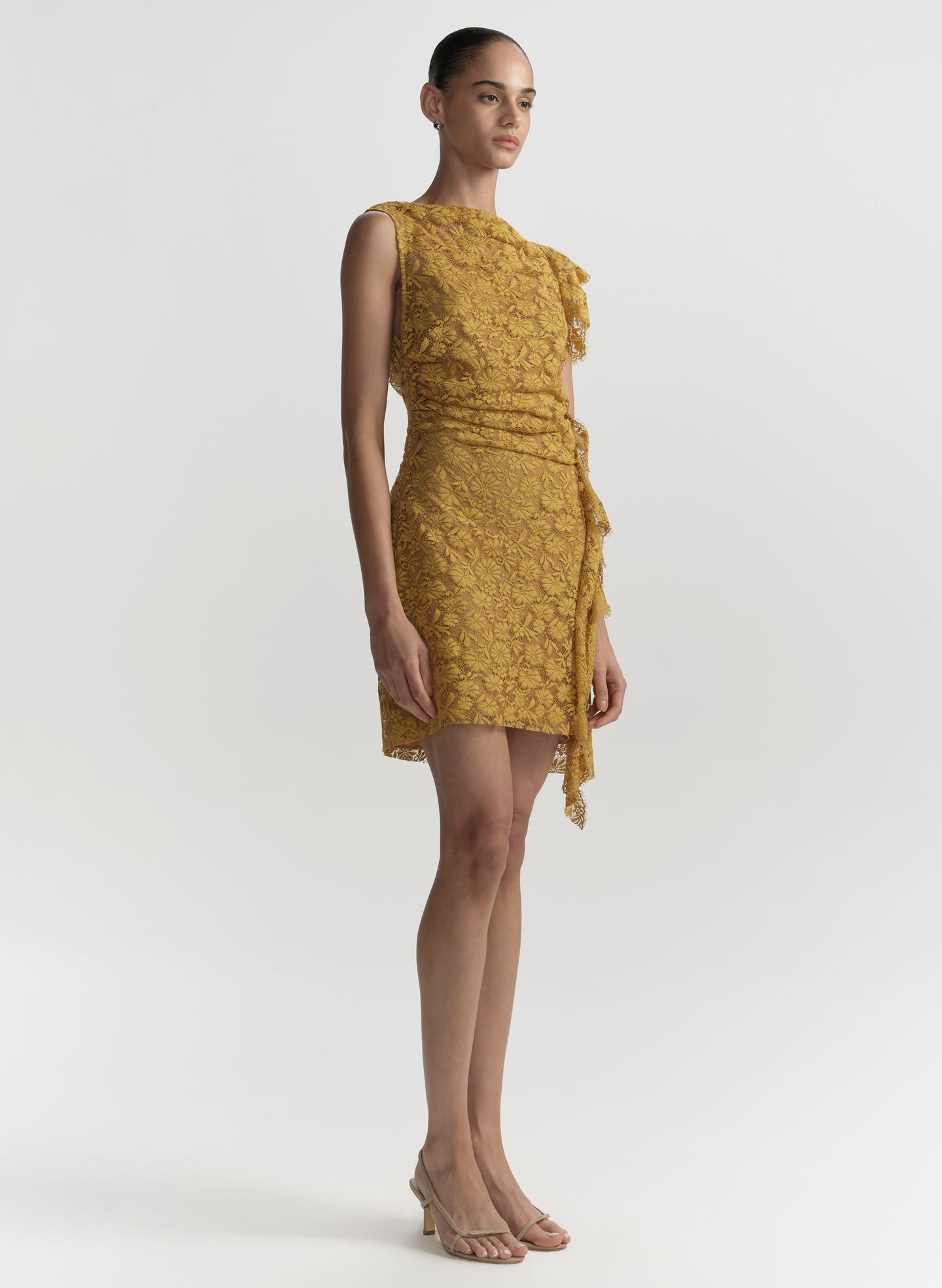 Woman wearing a mustard yellow lace dress on a white background