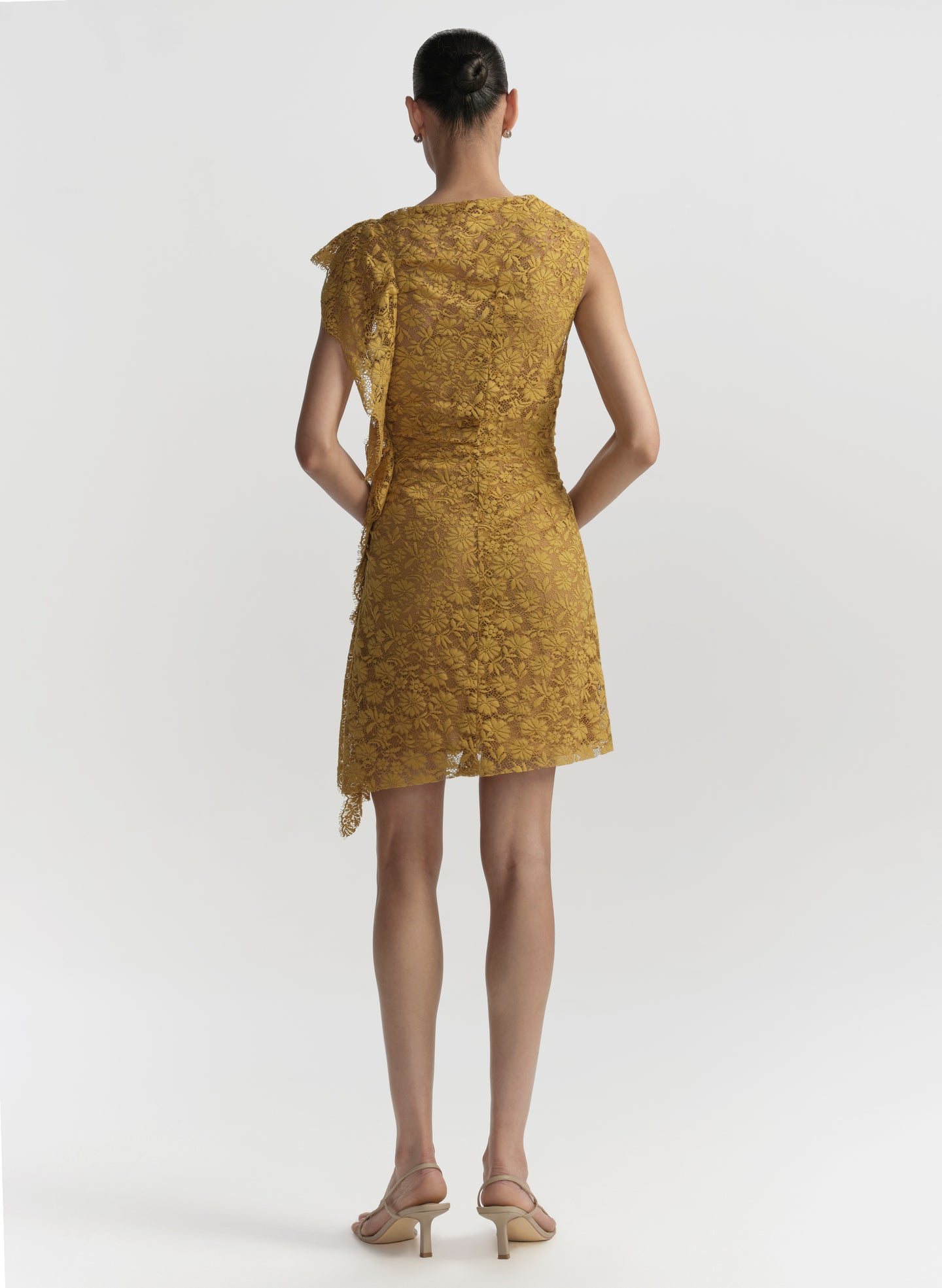 Woman wearing a mustard yellow lace dress on a white background