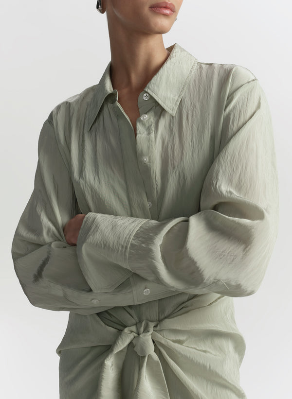 Person wearing a light green button-up shirt with a tie-waist design on a white background