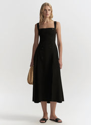 Woman wearing a black dress holding a brown handbag on a white background