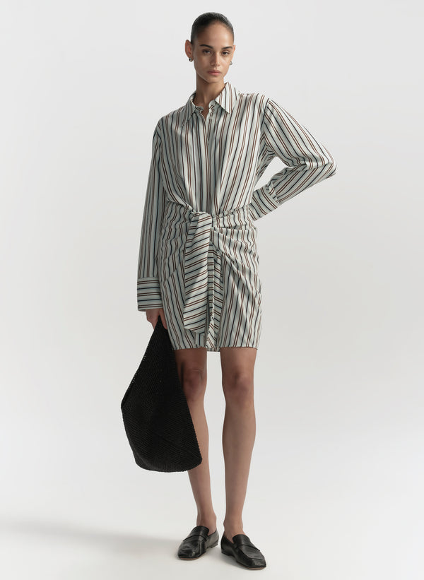 Woman wearing a striped shirt dress holding a black bag on a white background