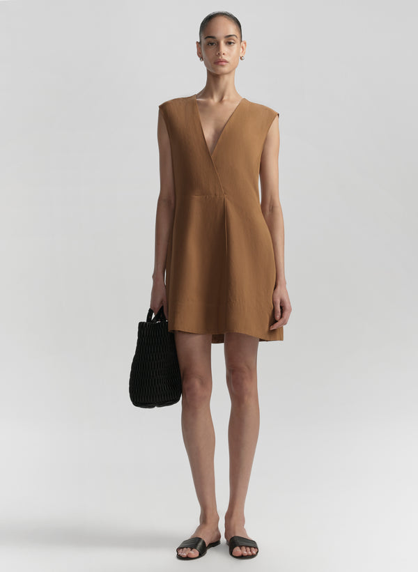 Woman wearing a brown dress holding a black handbag on a white background