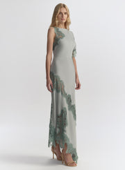 Woman wearing a long, elegant light blue dress with floral lace details on a white background