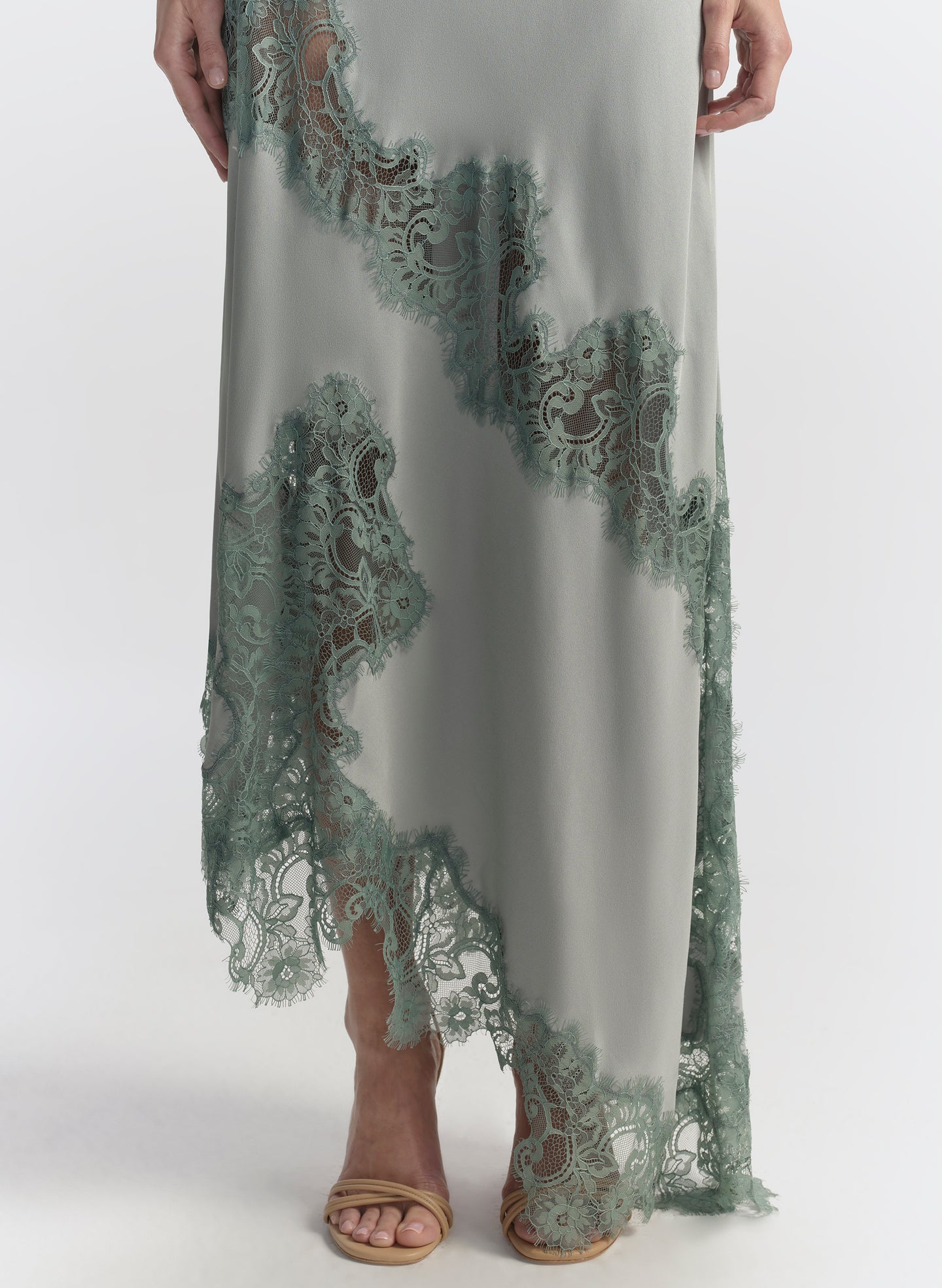 Woman wearing a long, elegant light blue dress with floral lace details on a white background