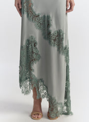 Woman wearing a long, elegant light blue dress with floral lace details on a white background