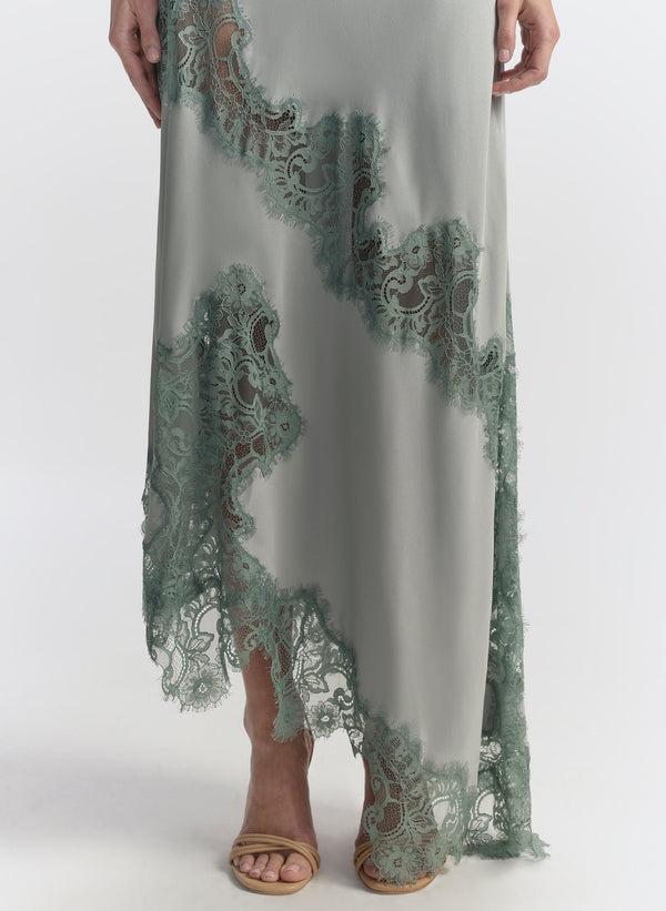 Woman wearing a long, elegant light blue dress with floral lace details on a white background