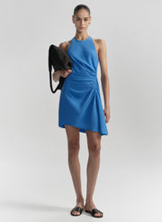 Woman wearing a blue dress holding a black clutch against a plain background