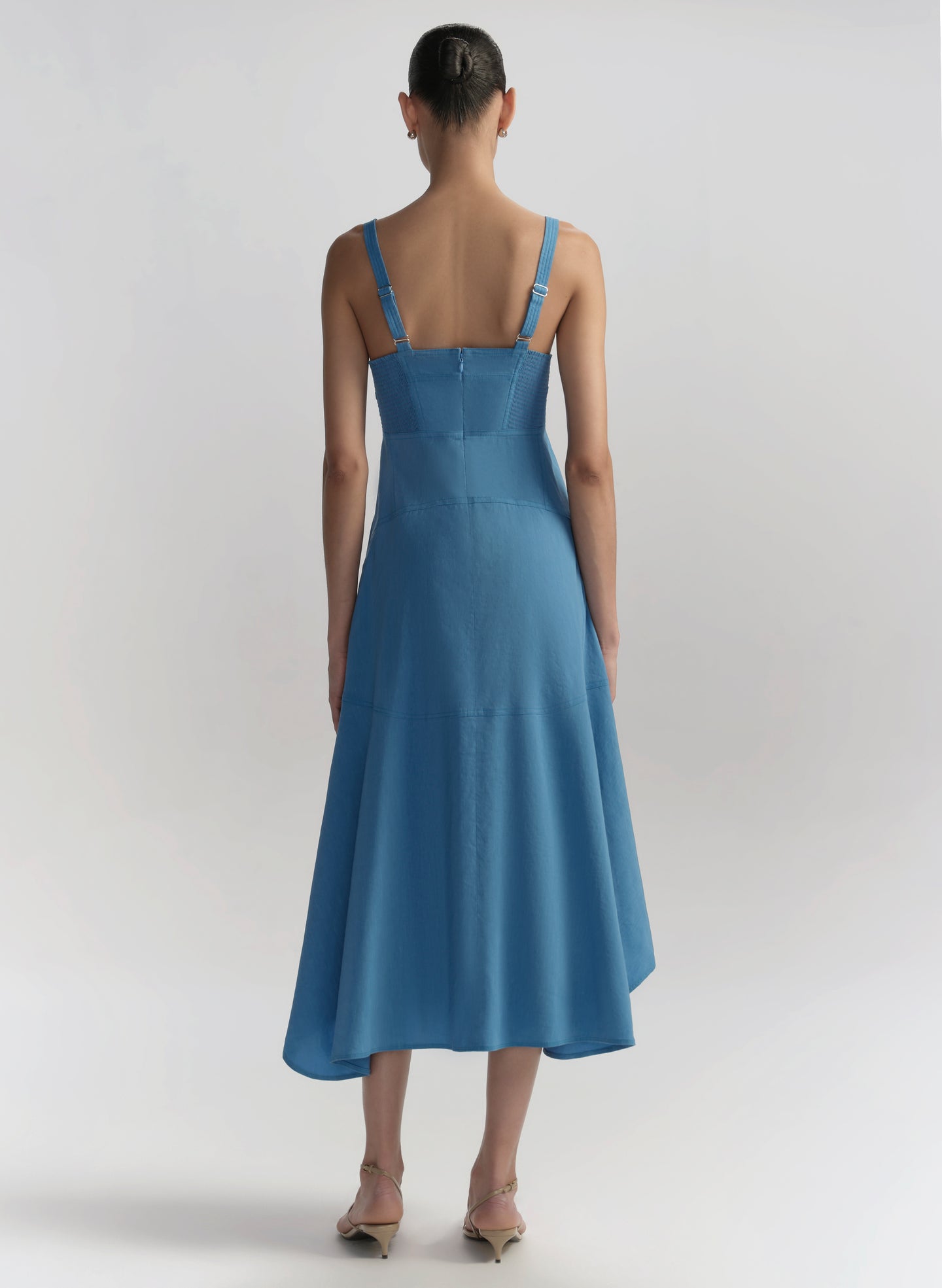 Woman wearing a blue dress with thin straps on a light gray background