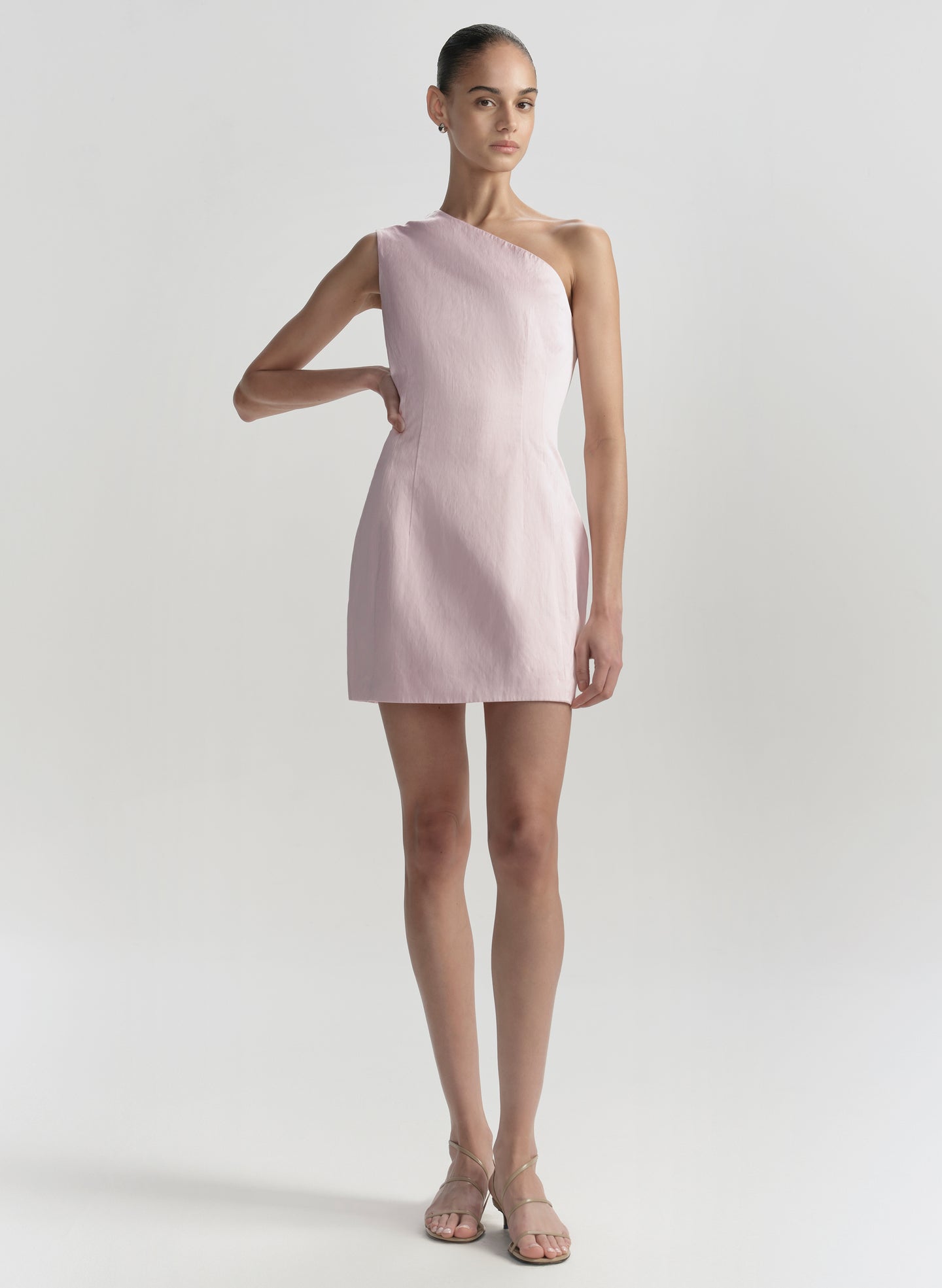 Woman wearing a light pink one-shoulder dress on a white background
