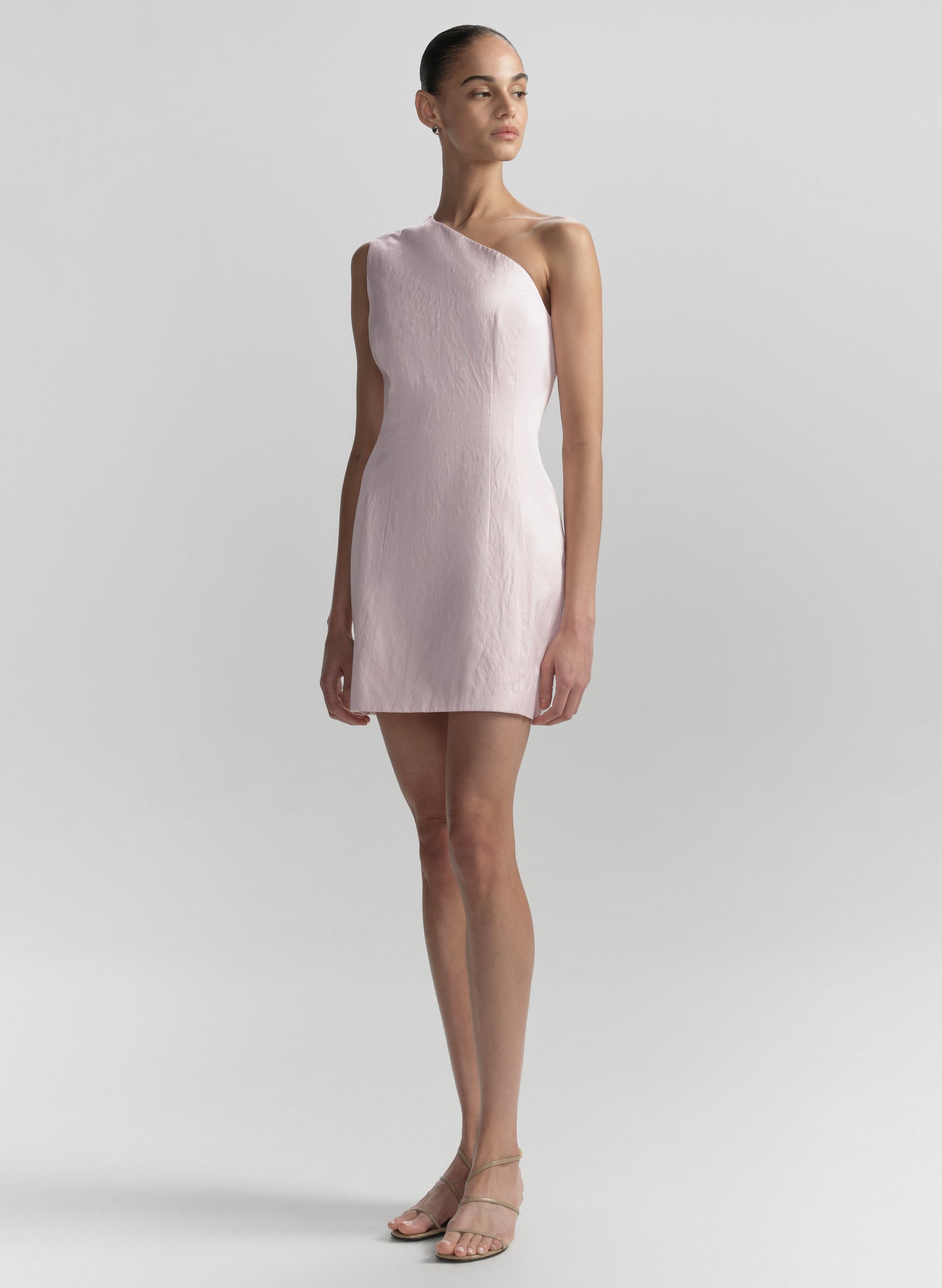 Woman wearing a light pink one-shoulder dress on a plain background