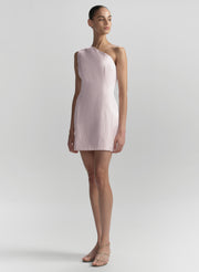 Woman wearing a light pink one-shoulder dress on a plain background