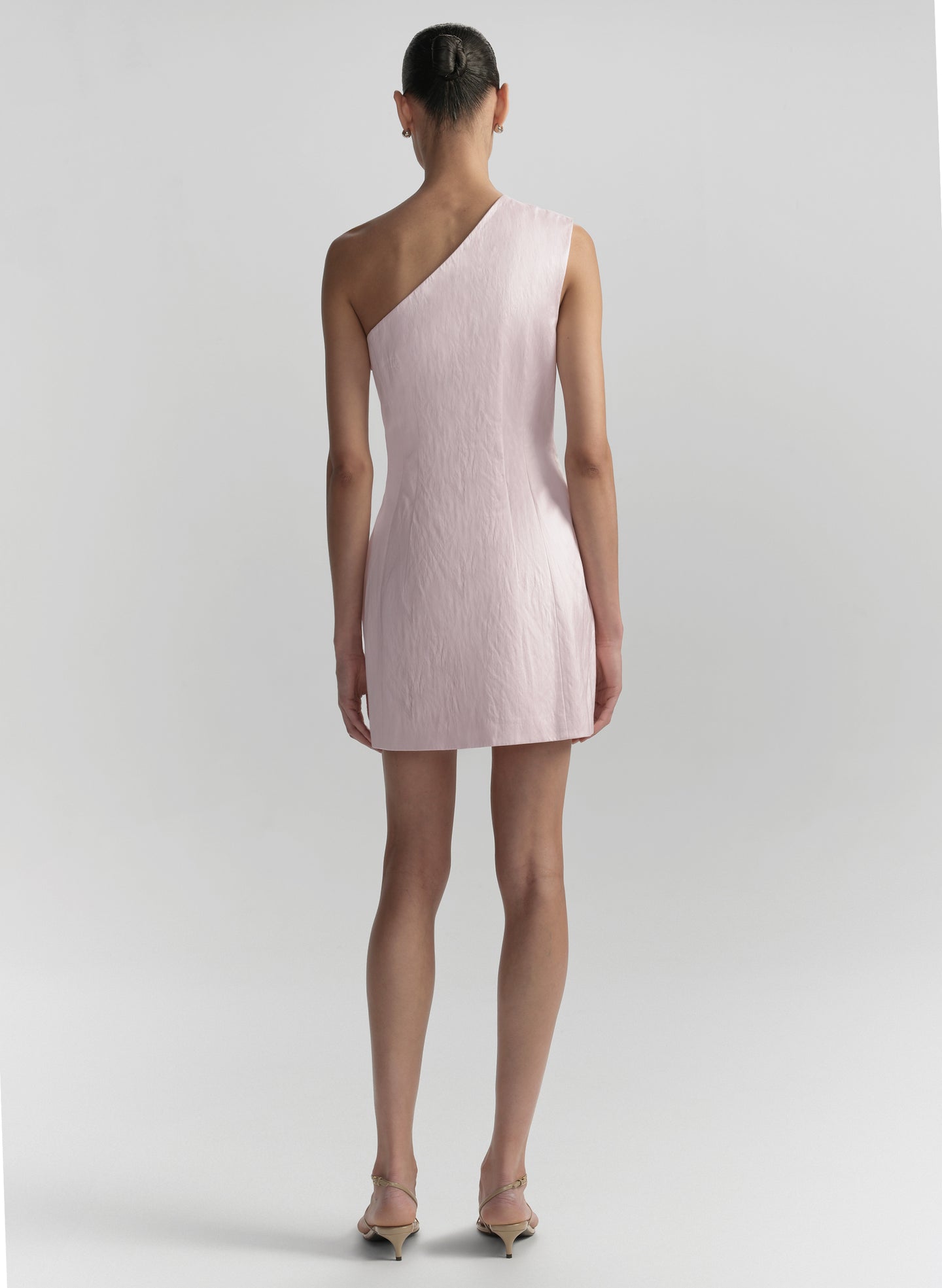 Woman wearing a light pink one-shoulder dress on a plain background