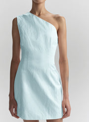 A model wearing a light blue crinkled one-shoulder dress against a neutral light gray background.