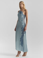 Woman wearing a long, light blue dress with floral lace details on a gray background