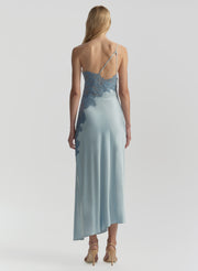 Woman wearing a long, light blue dress with lace detailing on a white background