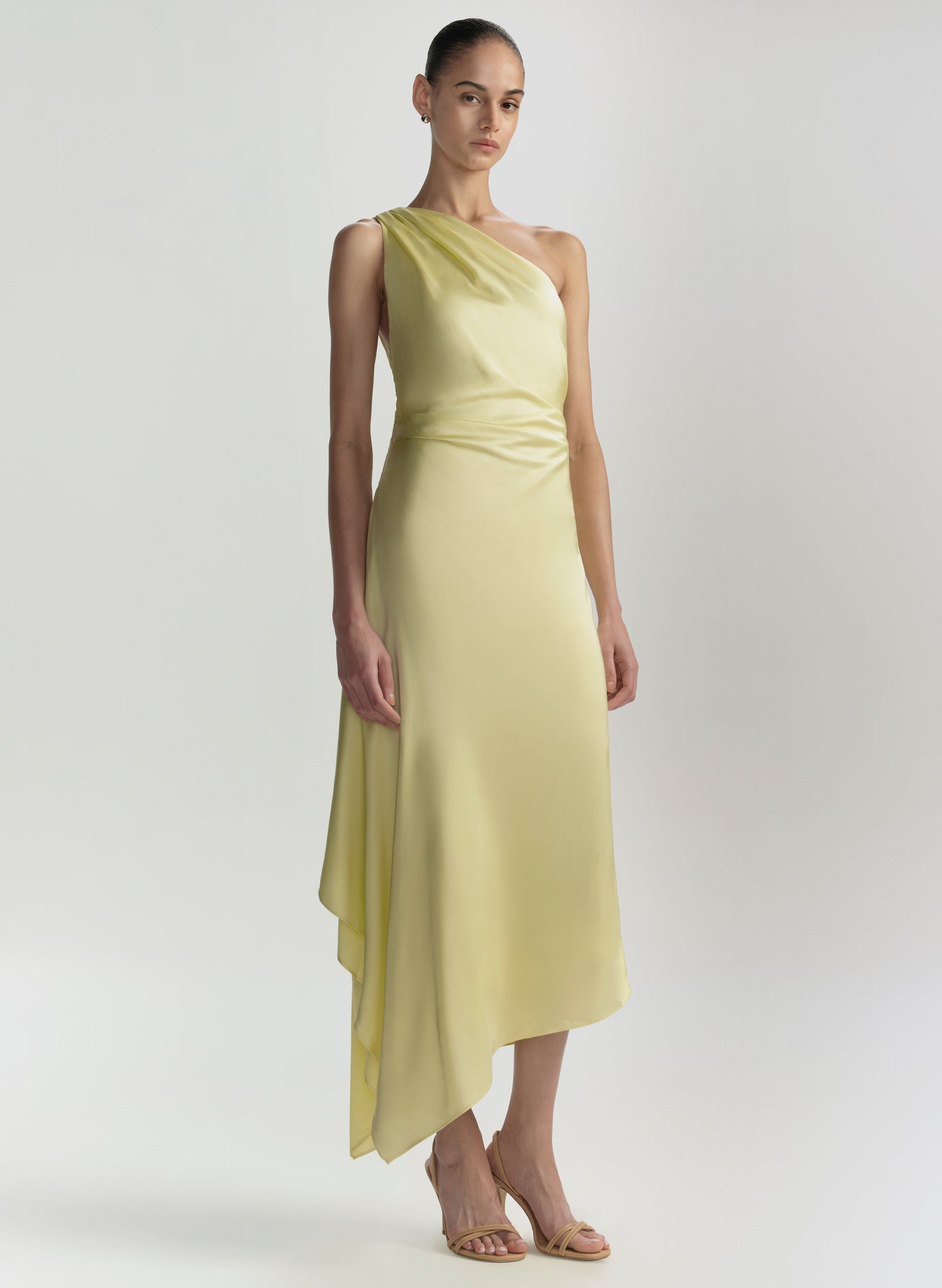 Woman wearing a light yellow one-shoulder dress on a white background