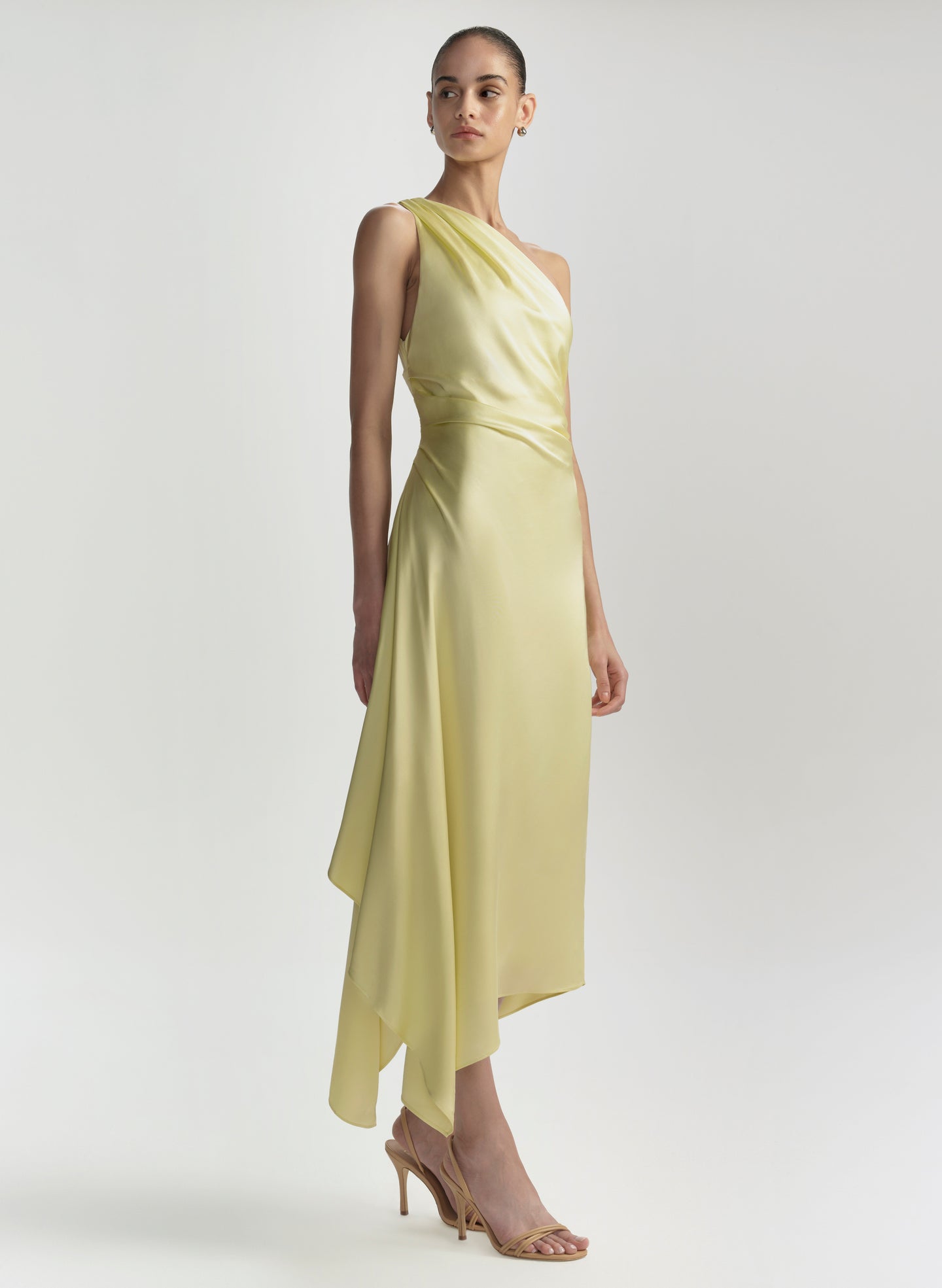 Woman wearing a light yellow one-shoulder dress on a white background