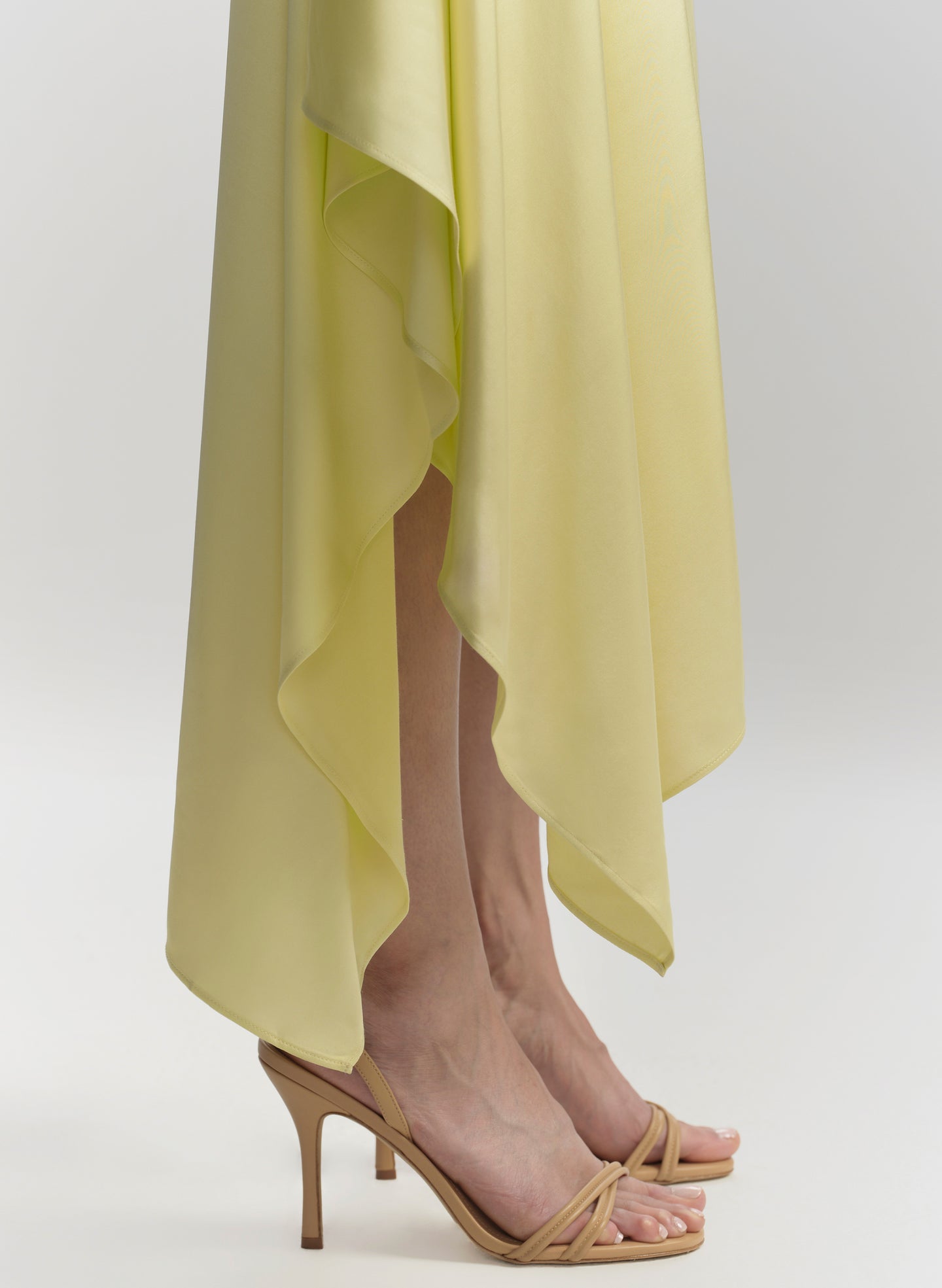 Yellow dress with high-low hem and beige high-heeled sandals on a white background
