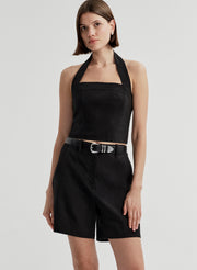 Woman wearing a black halter top and matching shorts with a belt on a light gray background