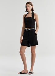 Woman wearing a black halter top and matching shorts with a belt on a light gray background