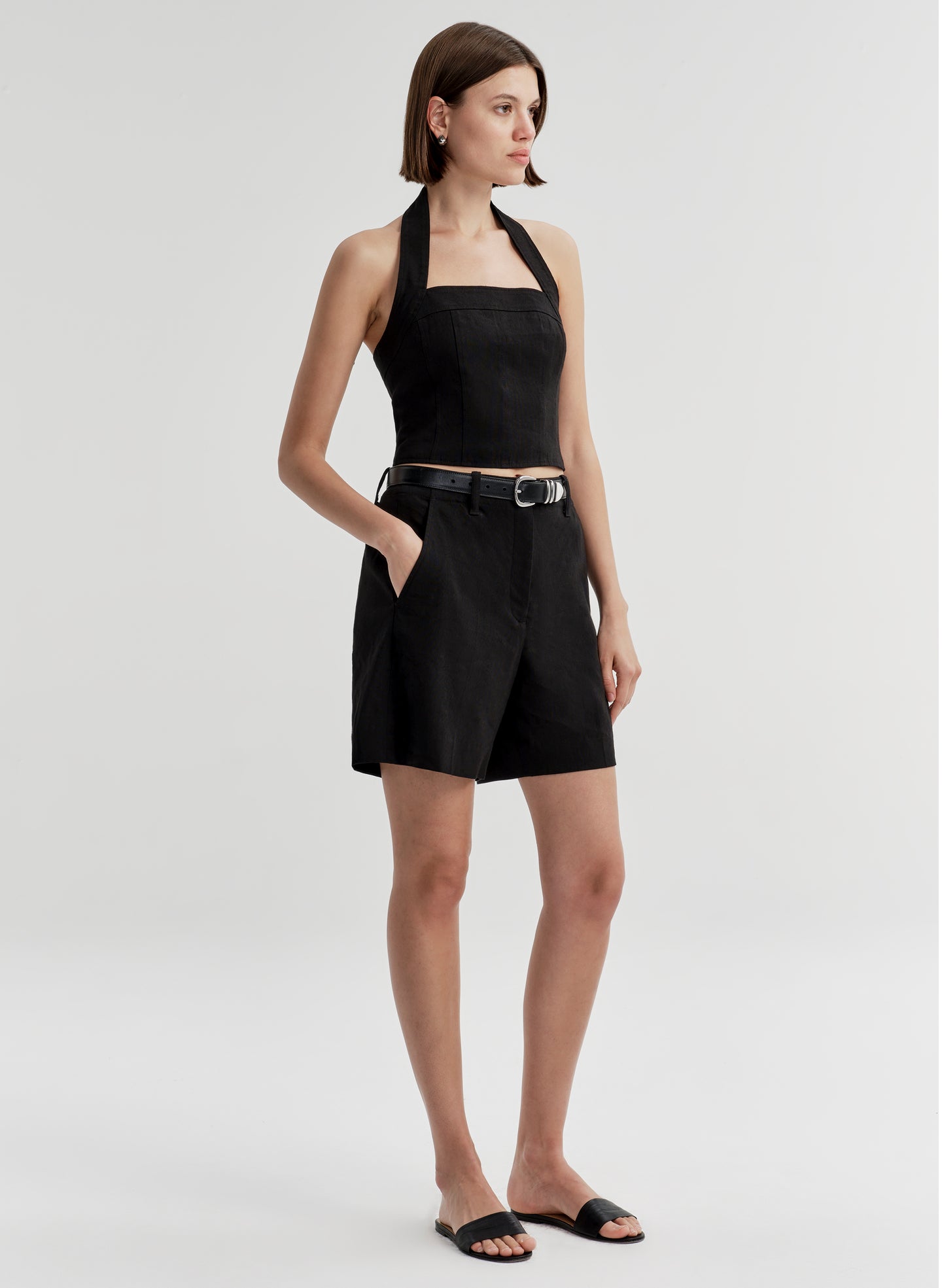 Woman wearing a black halter top and matching shorts with a belt on a light gray background