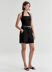 Woman wearing a black halter top and matching shorts with a belt on a light gray background