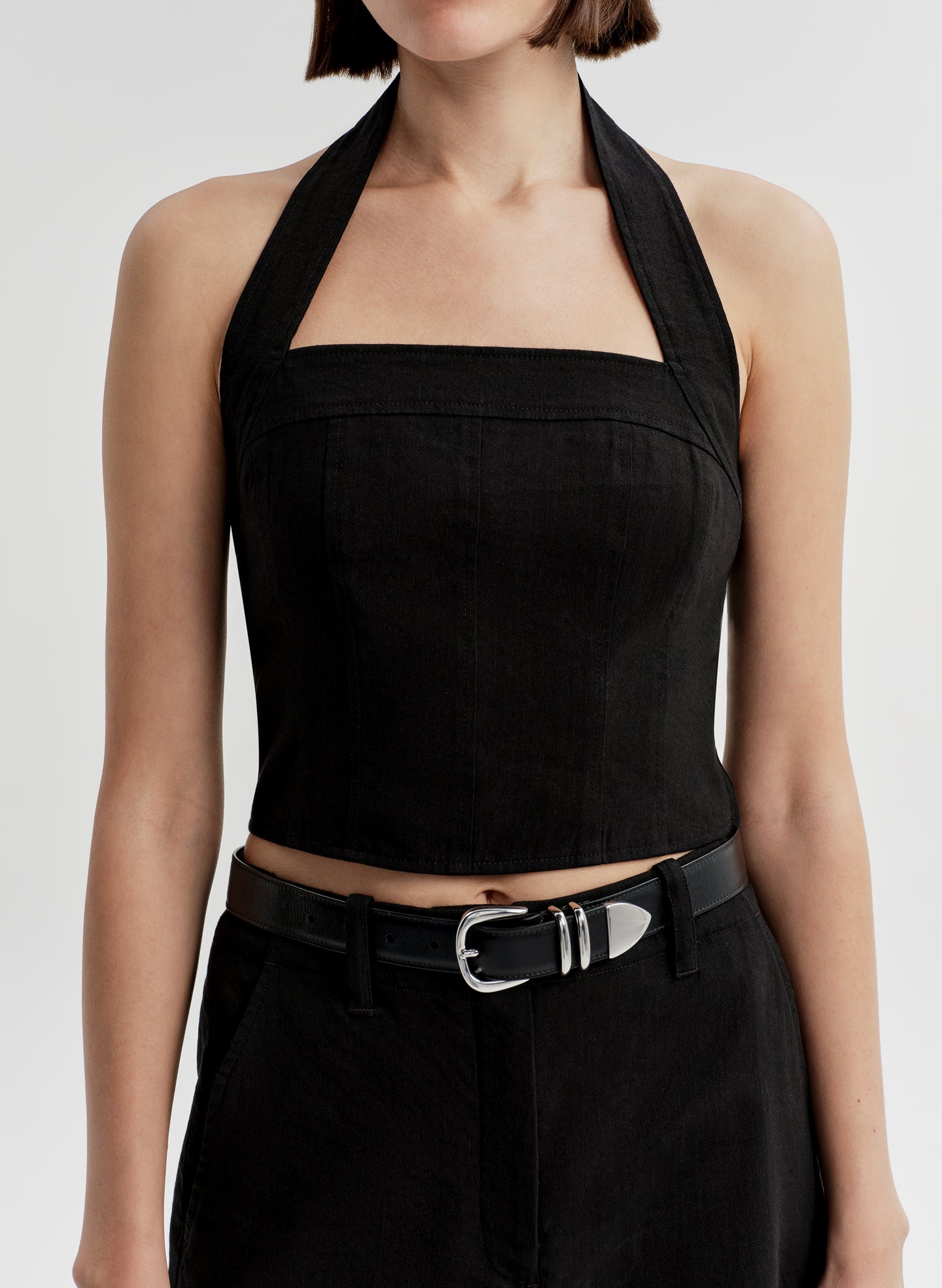 Woman wearing a black halter top and matching shorts with a belt on a light gray background