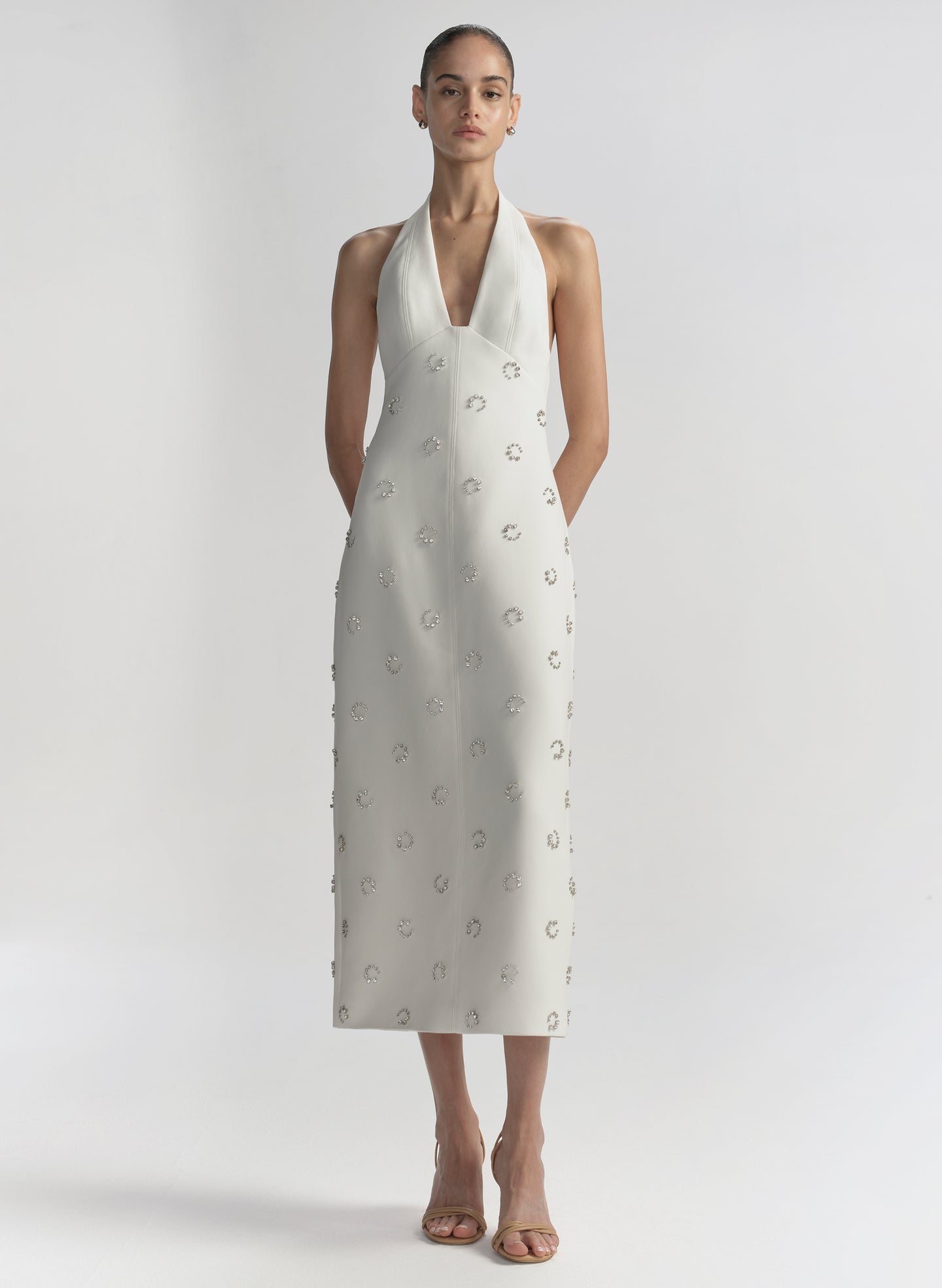 Woman wearing a white dress with embellished details on a plain background